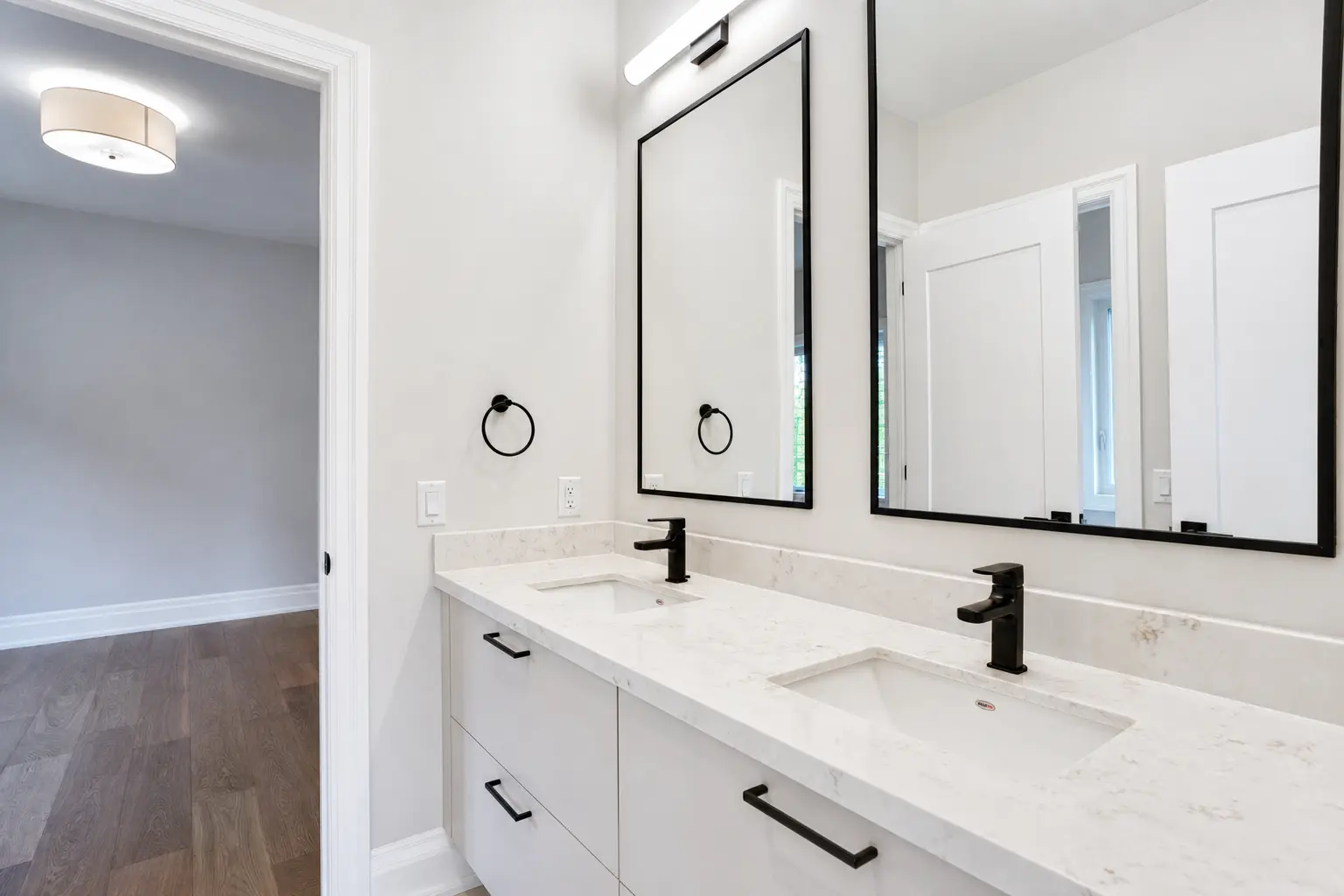 Bathroom with double vanity, twin mirrors and hardwood floors beyond