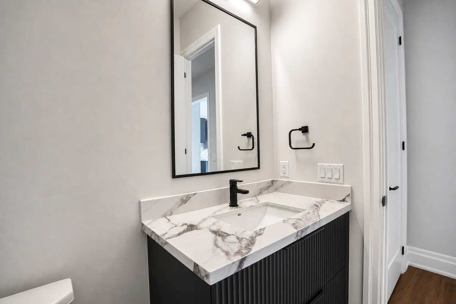 Powder room with fluted vanity, marble top and black framed mirror